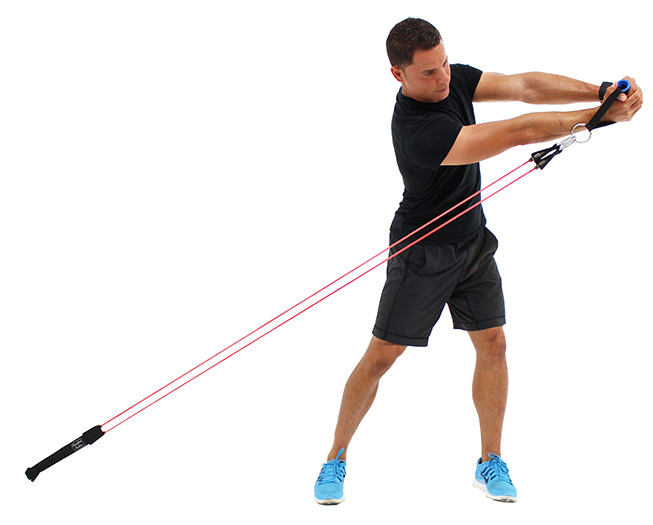 A man swings Bodylastics band handles across his body like a golf or baseball swing, against bands anchored low to the floor.