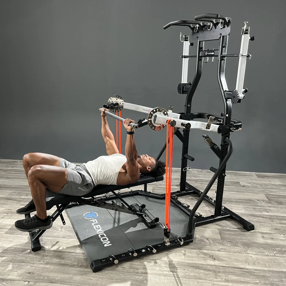 A man does a bench press on the FLEXICON tower, with orange Bodylastics bands clipped to the press arms.