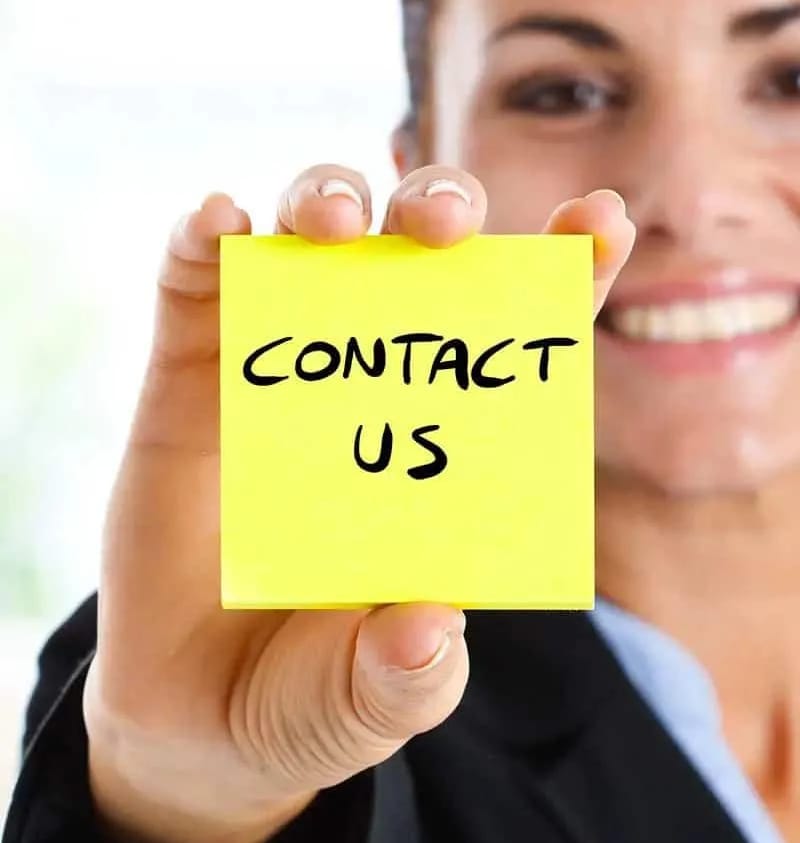 A smiling woman holds up a yellow sticky note that says Contact Us.