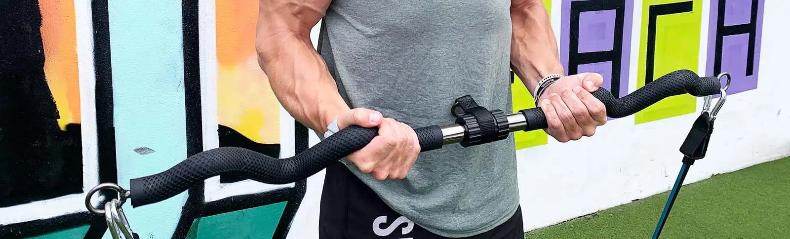 A man in a gray T-shirt curls the Bodylastics Resistance Bands Bar with bands clipped to each end.