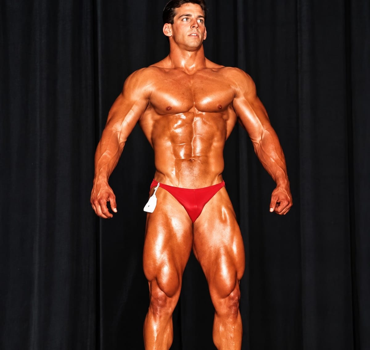 Blake at 21 on a bodybuilding stage, lean and muscular, in red posing trunks.