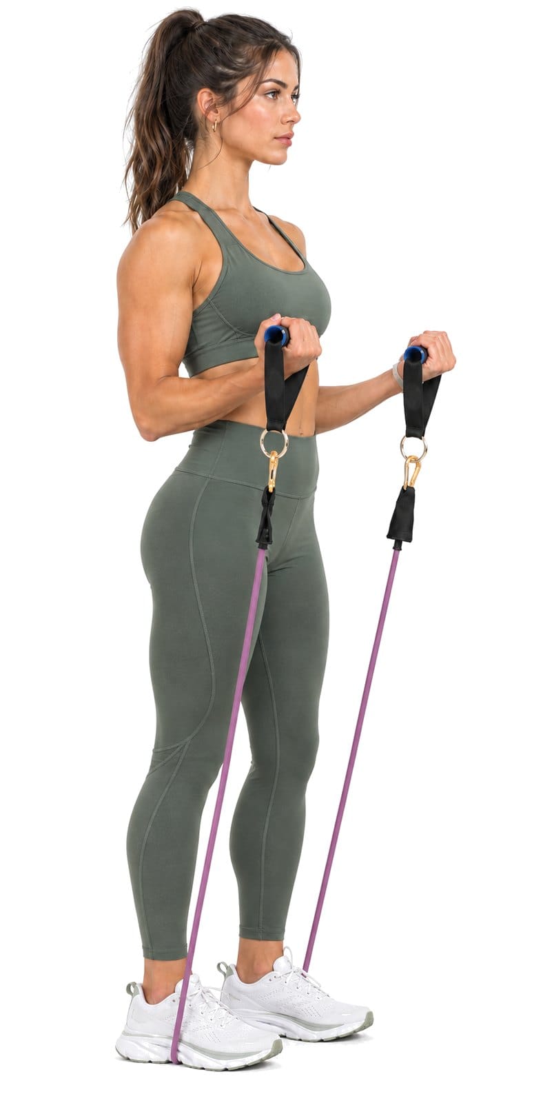 A woman stands on Bodylastics resistance bands and holds the handles at her waist with her elbows bent, ready to curl.